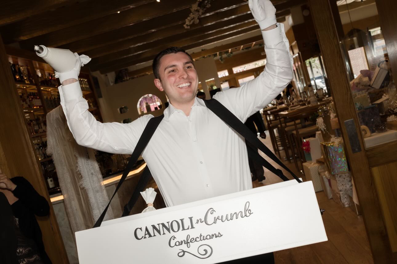 Arms raised with piping bags behind the Cannoli n Crumb strolling tray at a venue